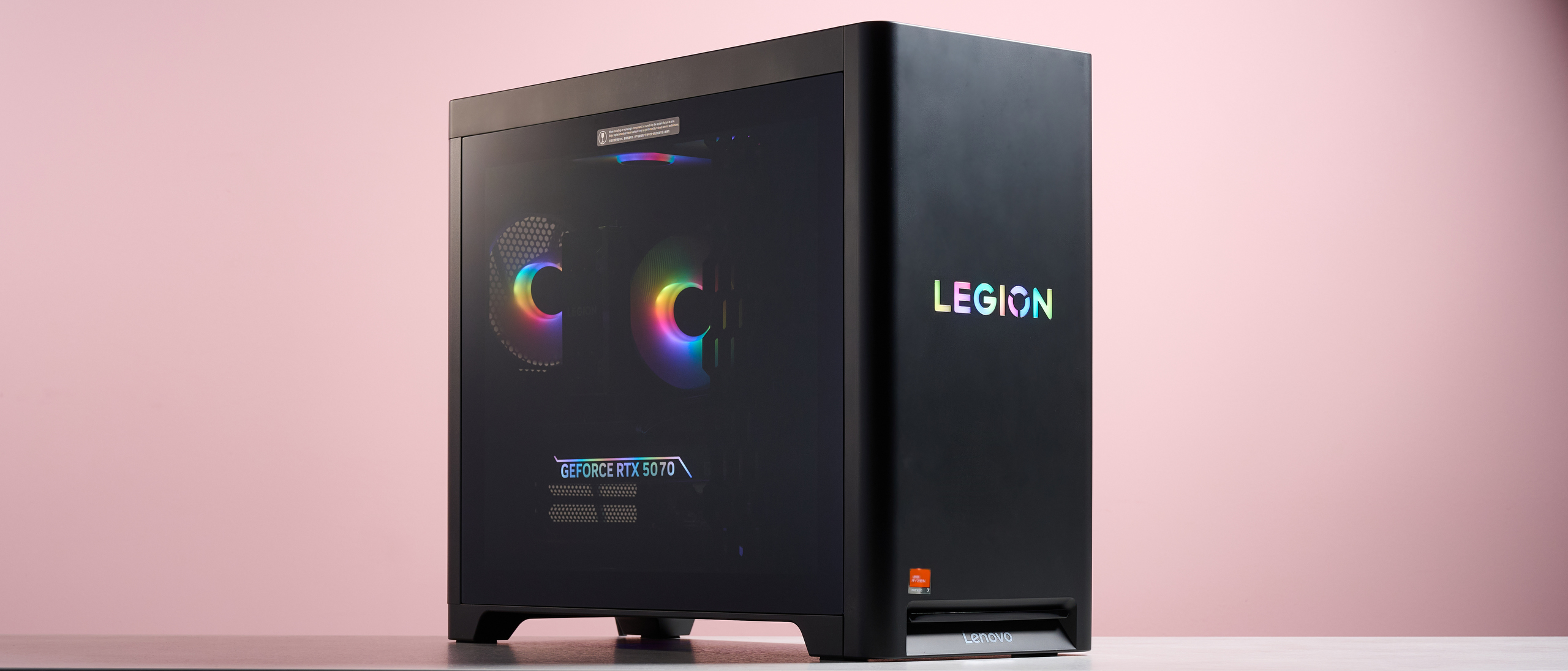 Three-quarter view of Lenovo Legion Tower 5 on desk with RGB lighting on, with pink wall in background