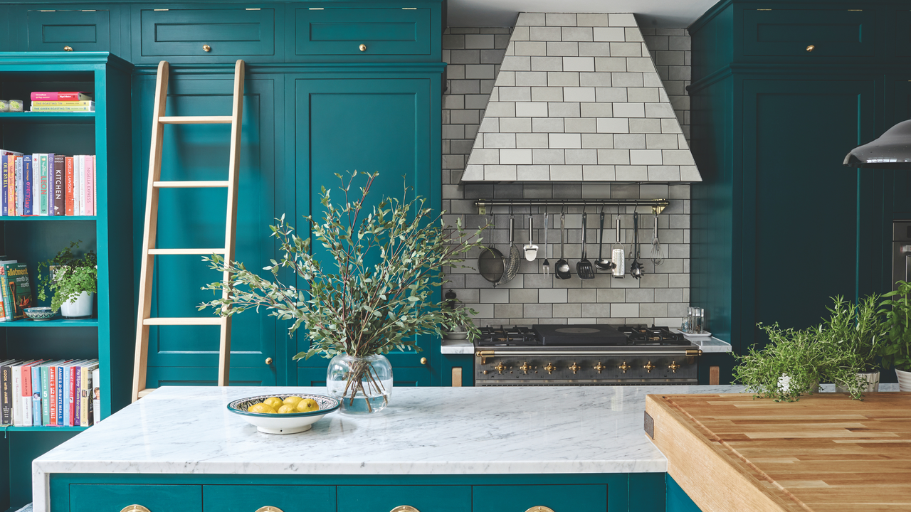 Modern, country kitchen with dark blue walls and units, kitchen island with white and grey marble top, range cooker with extractor tiled in grey. A renovated and extended six bedroom Victorian semi detached house in Beckenham, London, family home of Irem and Raj Patel and two children.