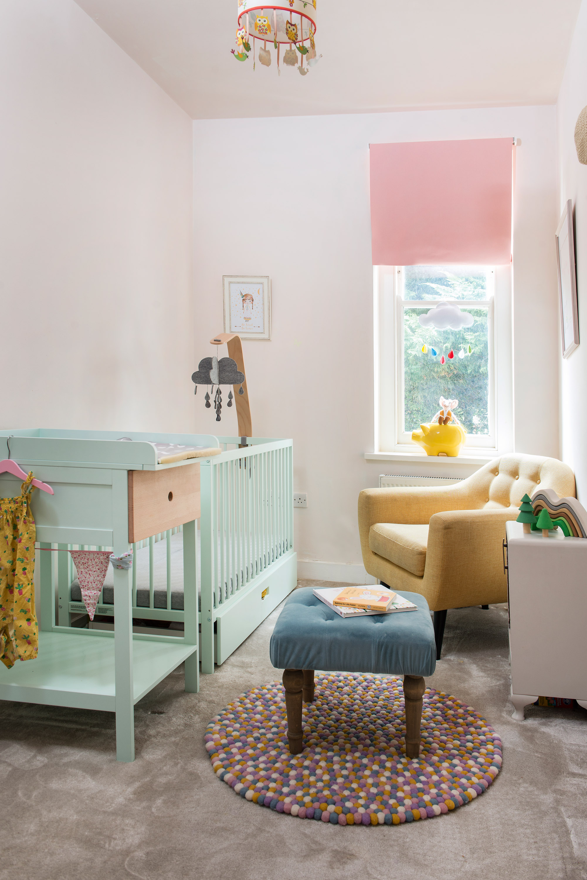 nursery with pastel colours, a yellow chair, blue stool, mint cot and pink blind