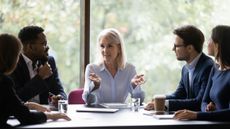 A mature female CEO speaking to a team of workers in a boardroom to represent workplace collaboration.