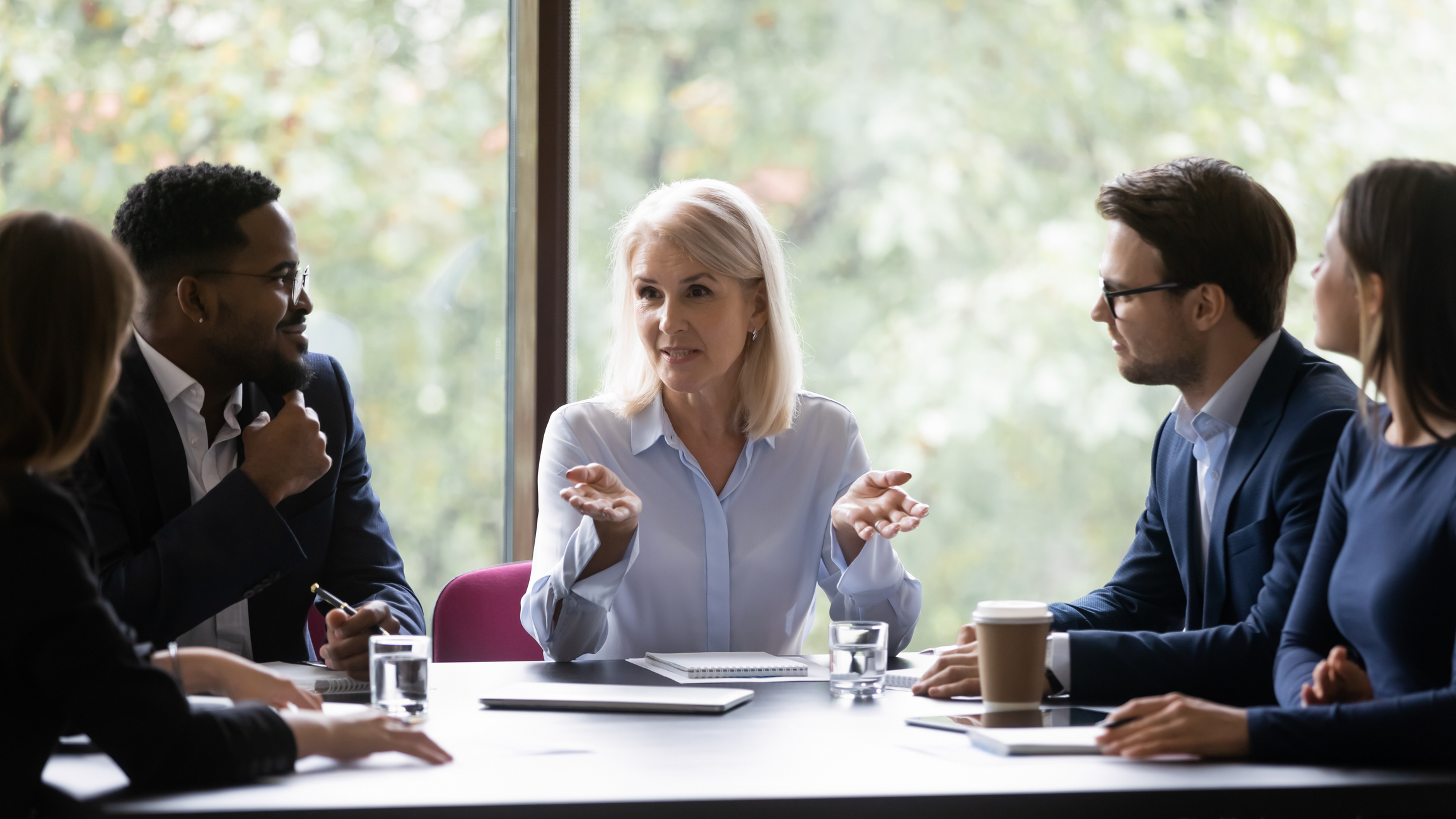 A mature female CEO speaking to a team of workers in a boardroom to represent workplace collaboration.