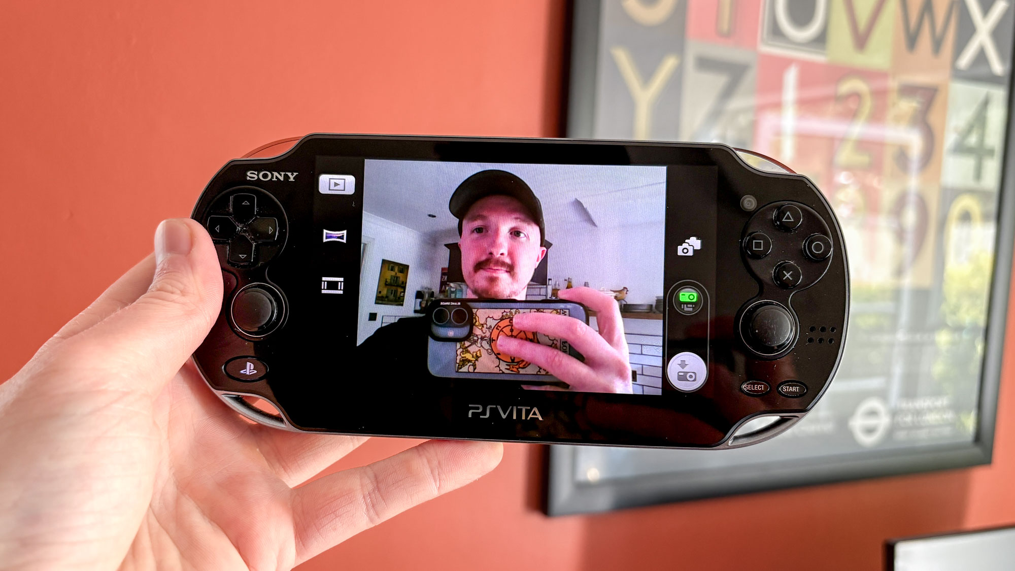 PS Vita in hand showing camera on display of person holding iPhone