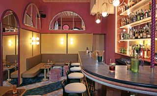 Bar, pink and mustard colour walls, bar counter with stools, bottles on shelves make for centerpiece