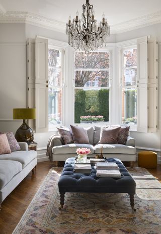 living room with wooden floor, gray sofas, blue footstool and crystal chandelier