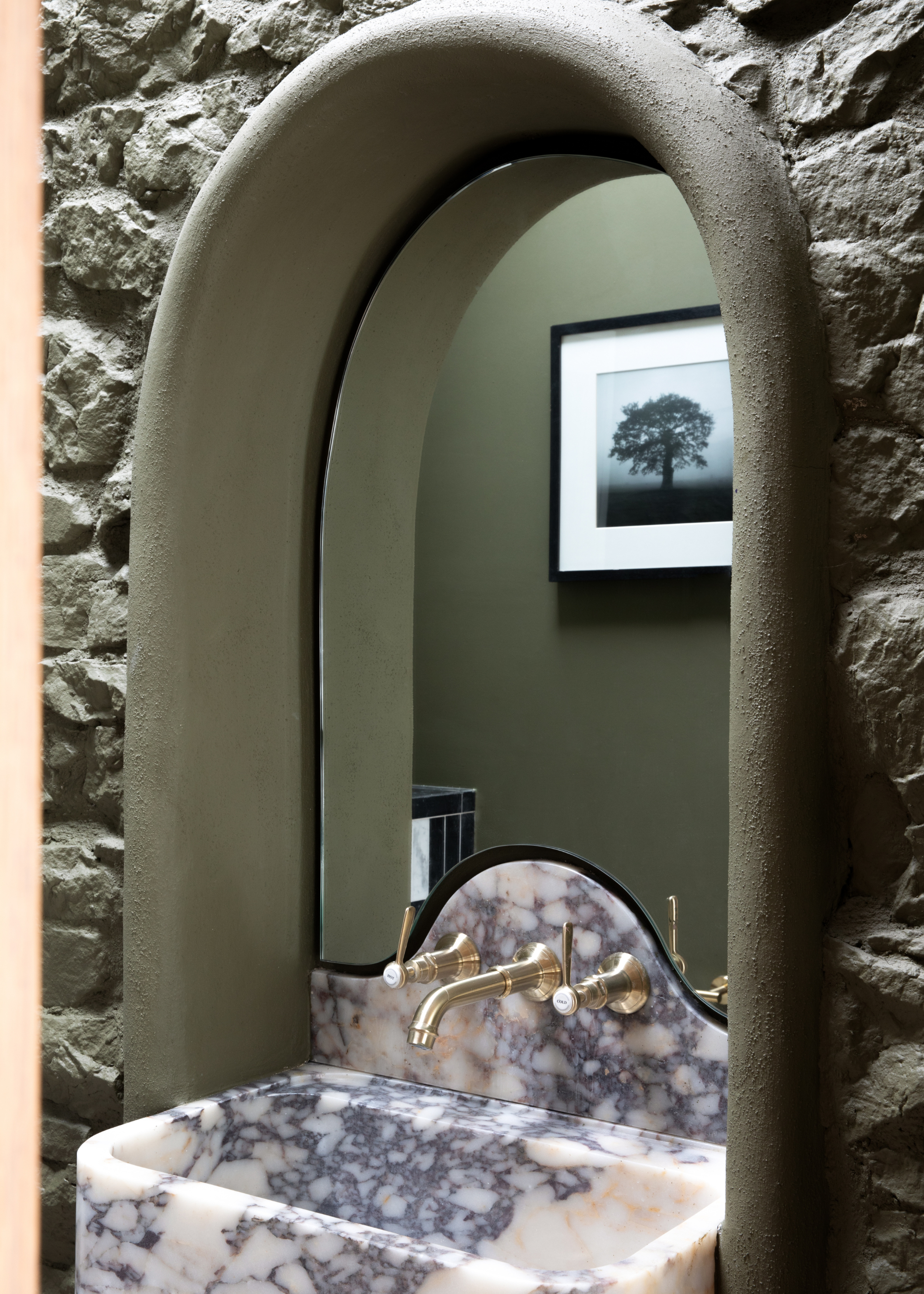 A cloakroom with a smooth arched mirror built onto the stone wall and a marble basin against it
