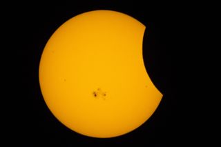 partial solar eclipse with the moon appearing to take a 'bite' out of the sun. A large sunspot is visible on the surface.