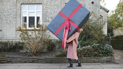 A woman carries a gift that's bigger than she is down the sidewalk.