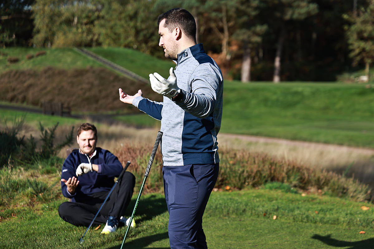 Nick Bonfield sitting on the ground checking his watch around the tee box, with Sam De'Ath throwing his arms up in frustration over slow play