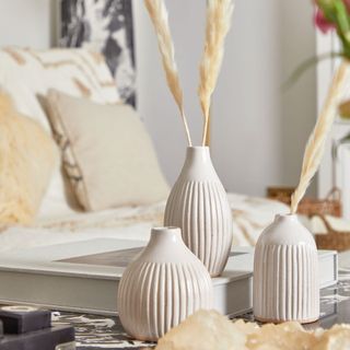 PrettyLittleThings white patterned vases on table with decorative reeds in next to white sofa