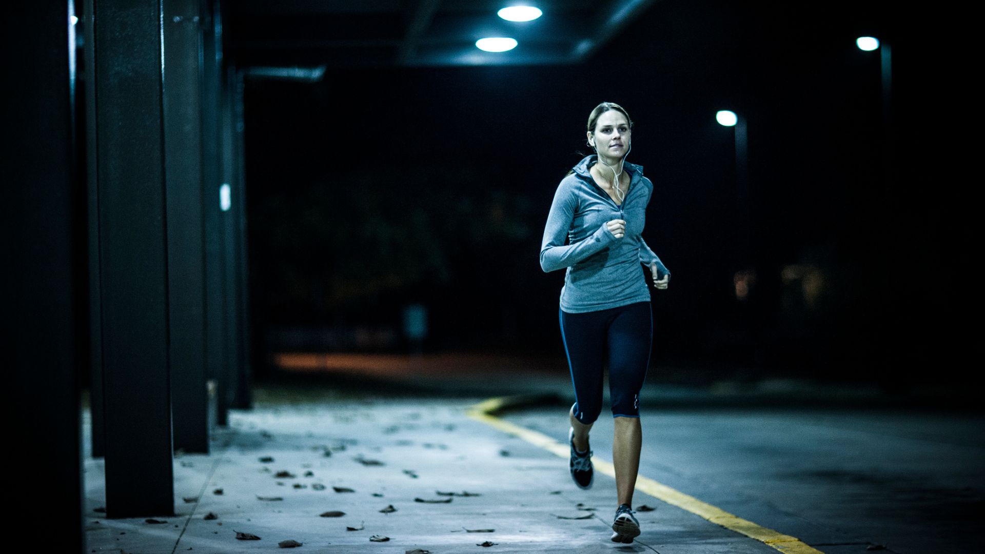 A woman running in a car park at night, lit up by street lights