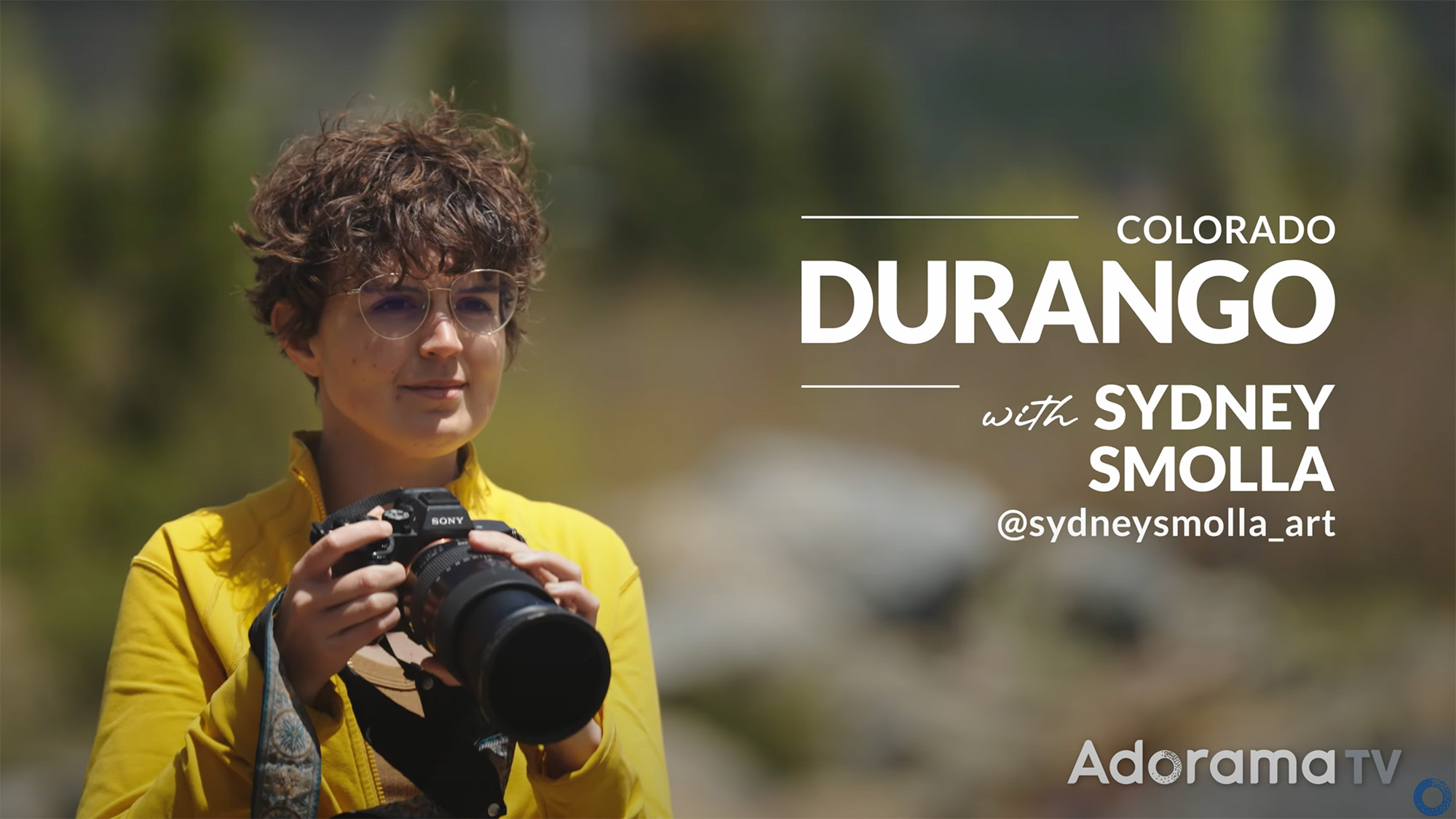 Screenshot of landscape photographer Sydney Smolla from Adorama's Picture America video series, showing her with a white jacket holding a Sony camera 