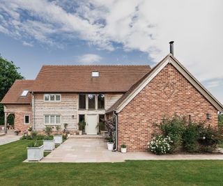 A stunning two-storey detached cottage made of timber frame and oak construction the patio and gardens are thoughtfully landscaped with potted trees lining the edges of the patio. There is a red bricked portion of the house as well as a timber clad area