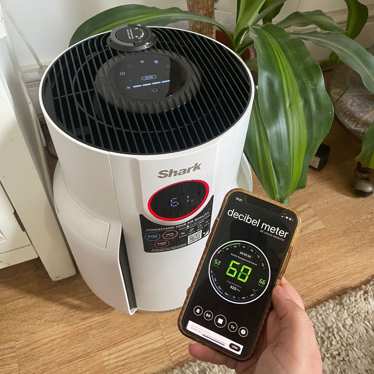 Hand holding a phone with a decibel meter on it in front of the Shark NeverChange 5 Air Purifier