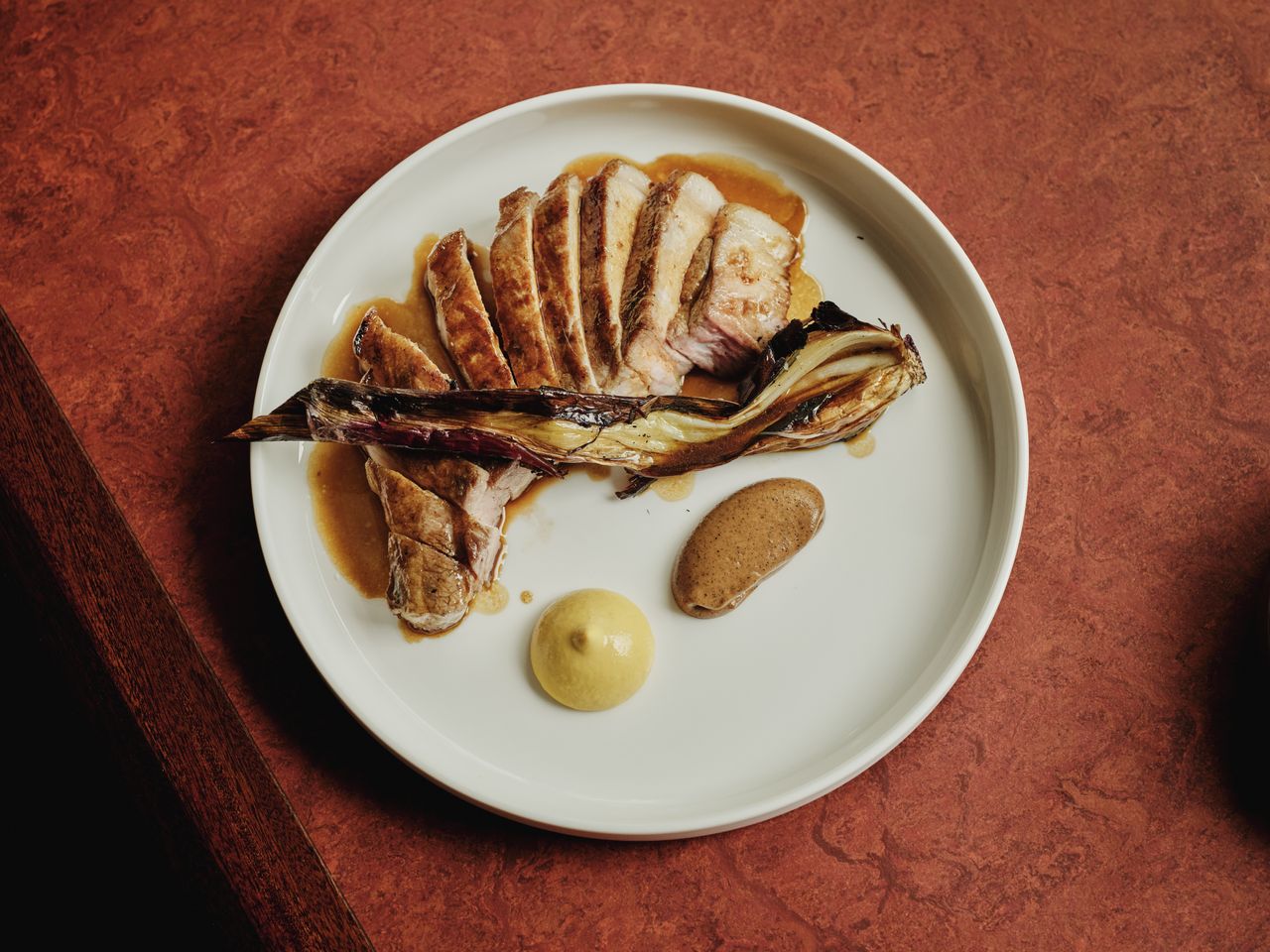 Aerial view of a shallow plate onto which rests a pork fillet with mustard and creamy, brown glazing.