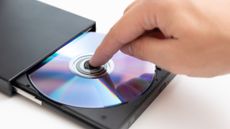 Someone's finger holding down a DVD disk in an external DVD player