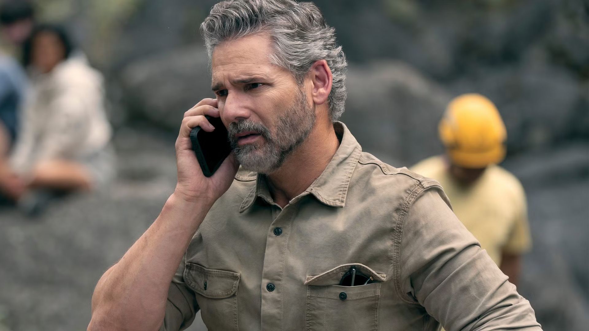 Eric Bana talks on the phone while a crime scene is cleared up behind him