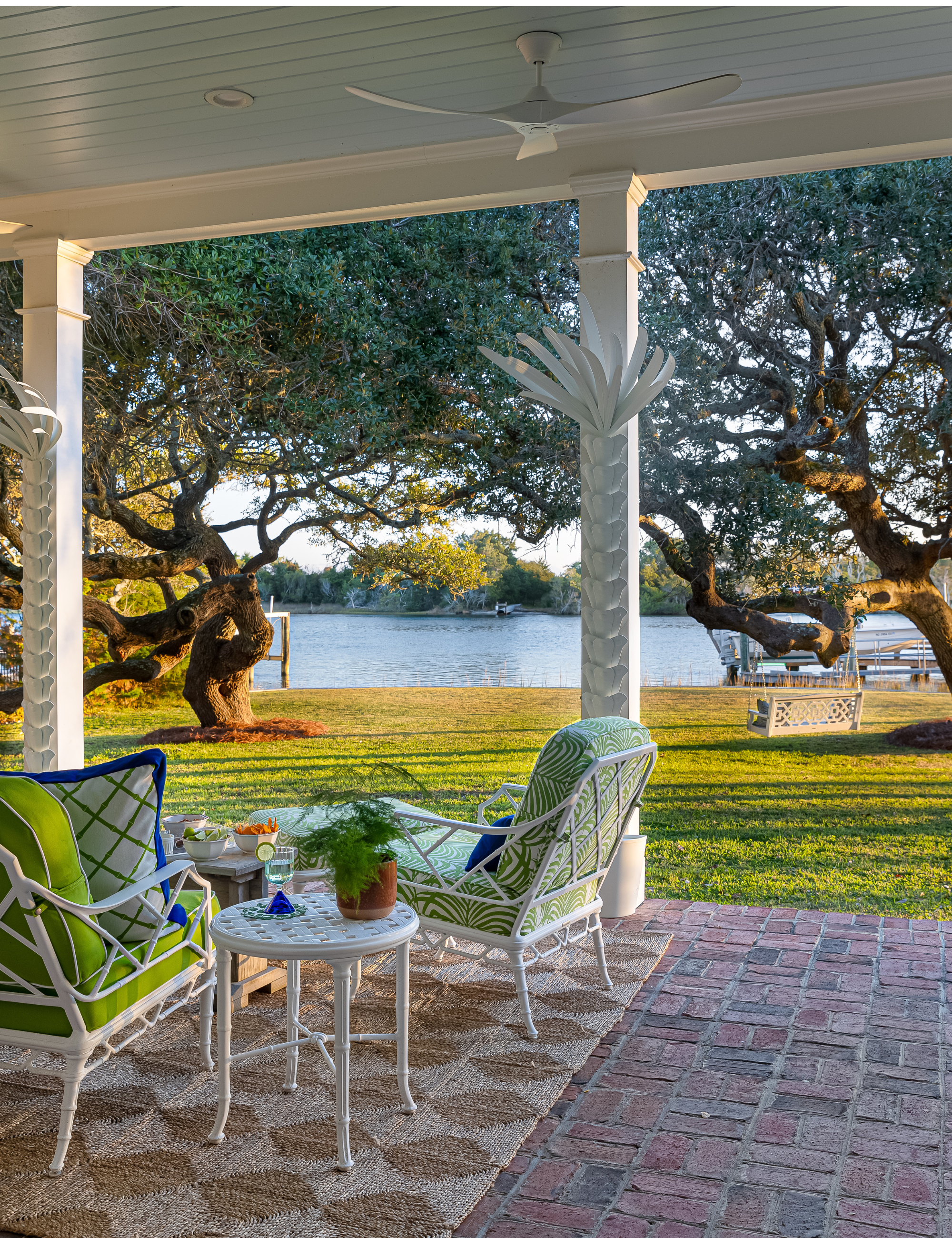Charming lakeside brick patio styled with a geometric jute rug, personality-packed patio seating group, and monochromatic white fans and light fixtures overhead.