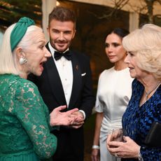 David and Victoria Beckham looking on as Helen Mirren, in a green lace gown, talks to Queen Camilla in a blue evening dress