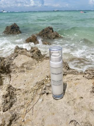 A bottle of Josh Rosebrook Nutrient Day Cream sitting on the beach.