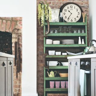 A kitchen with a vintage open green cupboard and large clock on top