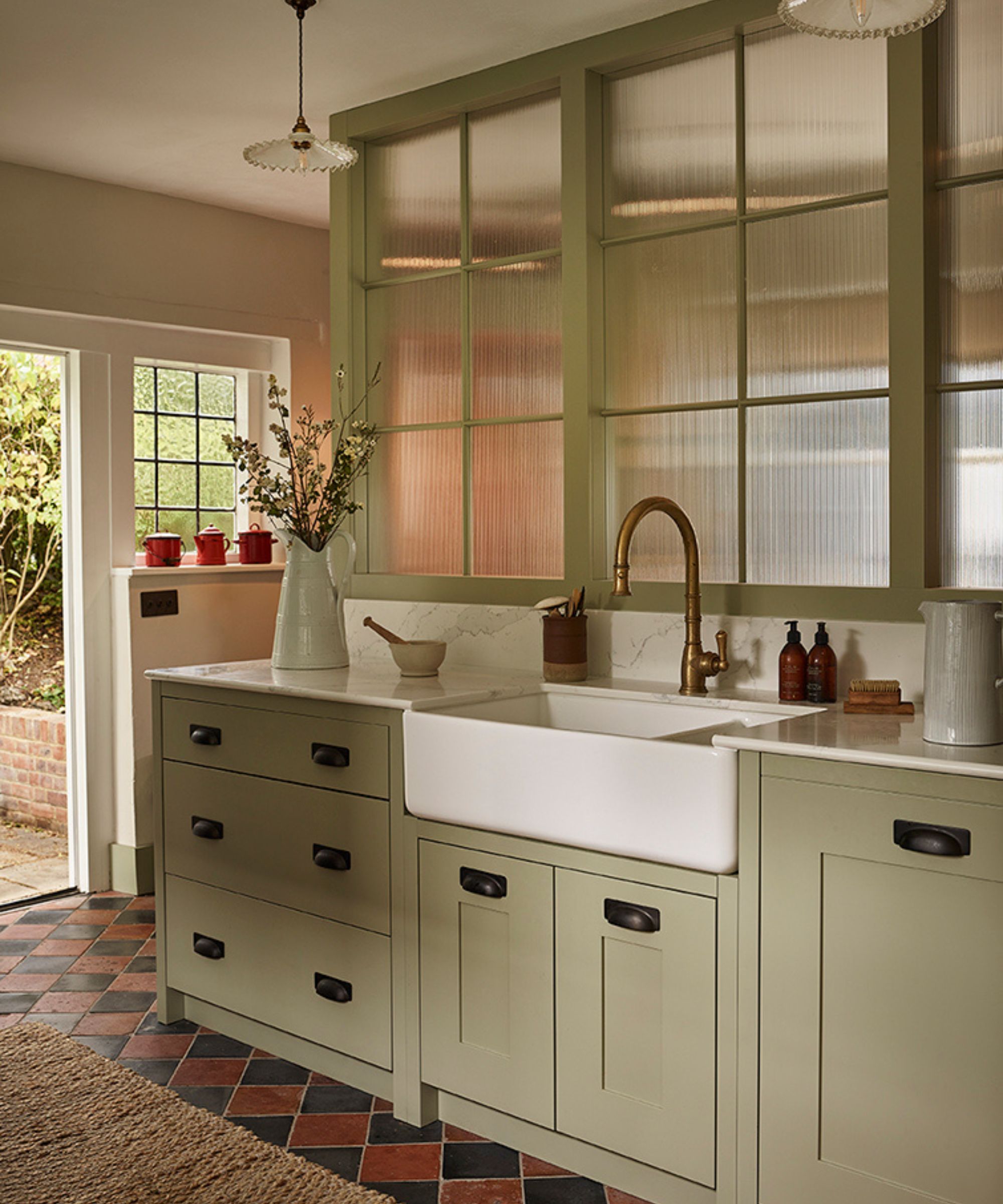 a pale green small kitchen sink area with a glass partition wall, and red and black quarry tile checkerboard floor