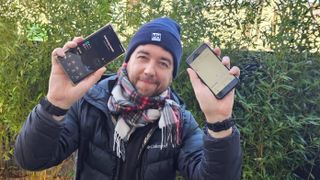 Journalist outdoors showing step trackers on two phones to the camera