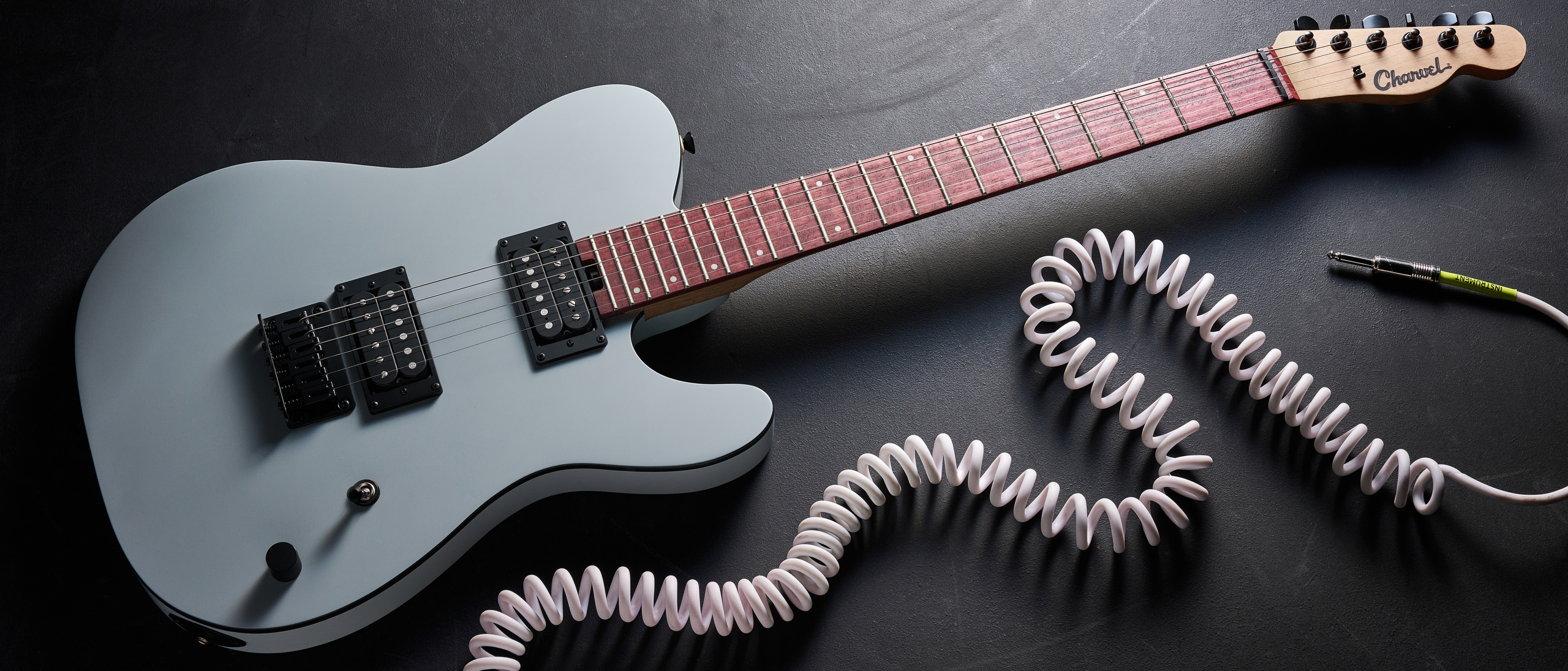 A Charvel Standard Series San Dimas Style 2 SD2 HH HT electric guitar lying on a dark floor with a coiled guitar cable next to it