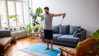 Man watching online videos and doing exercise with resistance bands at home