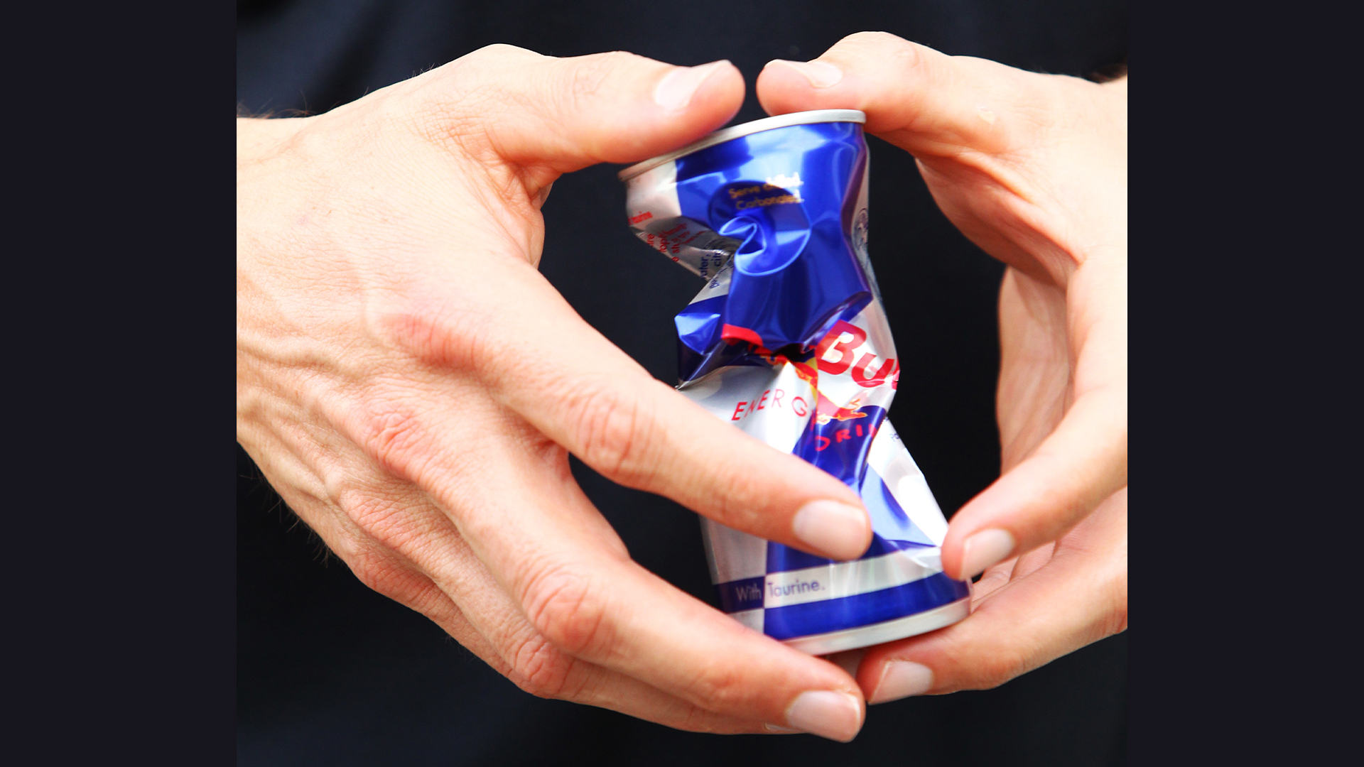 Crushed Red Bull can in a person's hands 