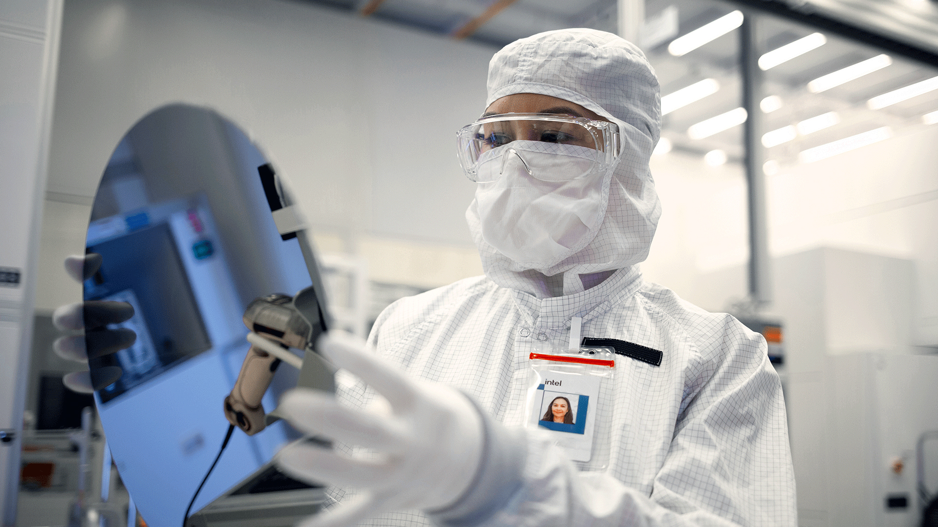 An Intel Foundry engineer in clean room gear holds a silicon wafer at an Intel facility in Chandler, Arizona.