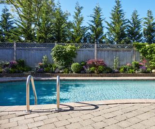 Backyard pool with a wooden fence behind and well-laid paver patio surrounding