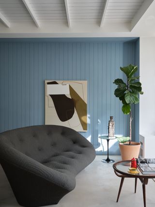 A living room with panelled walls painted in a light powdery blue with a black curved sofa