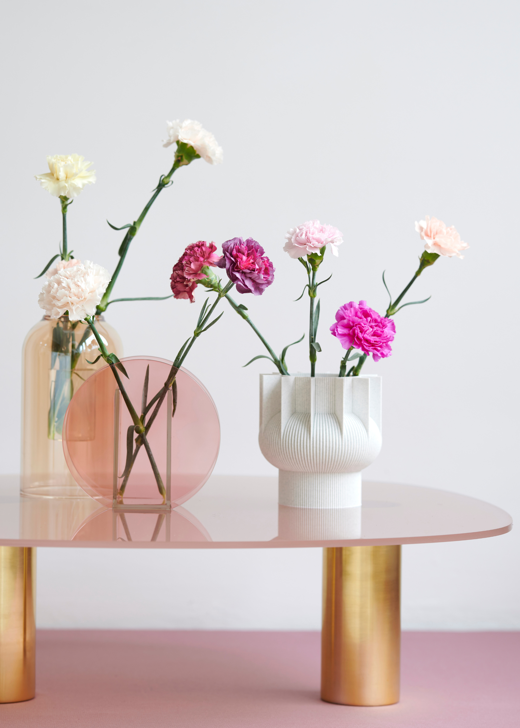 A trio of vases with white and pink carnations on a low-slung coffee table