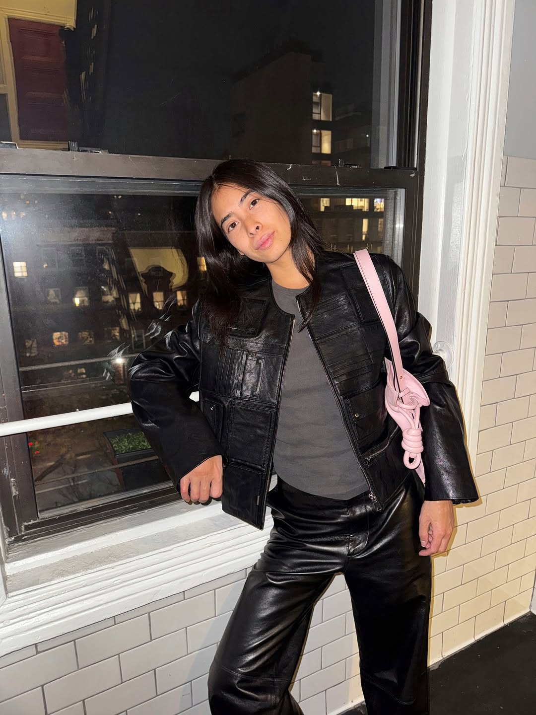 A woman wears a light pink shoulder bag with a leather jacket and pants.