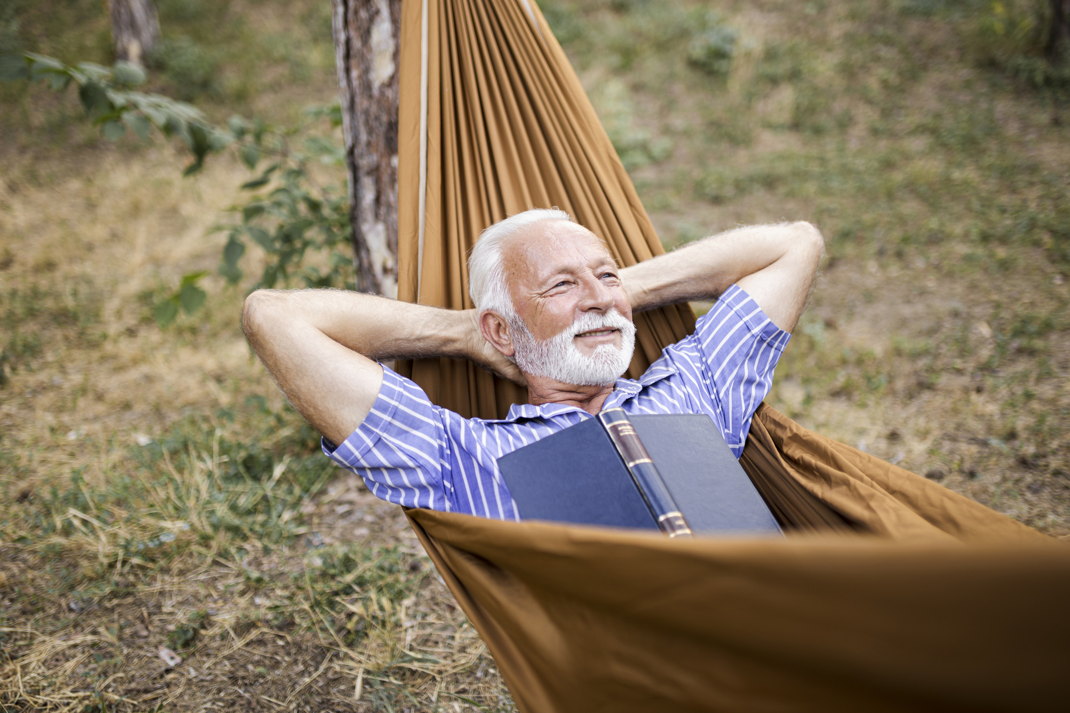 Senior man laying on hammock in nature and reading book
