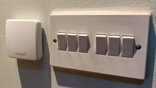 The screenless thermostat of the Wunda WundaSmart positioned on a wall next to a light switch