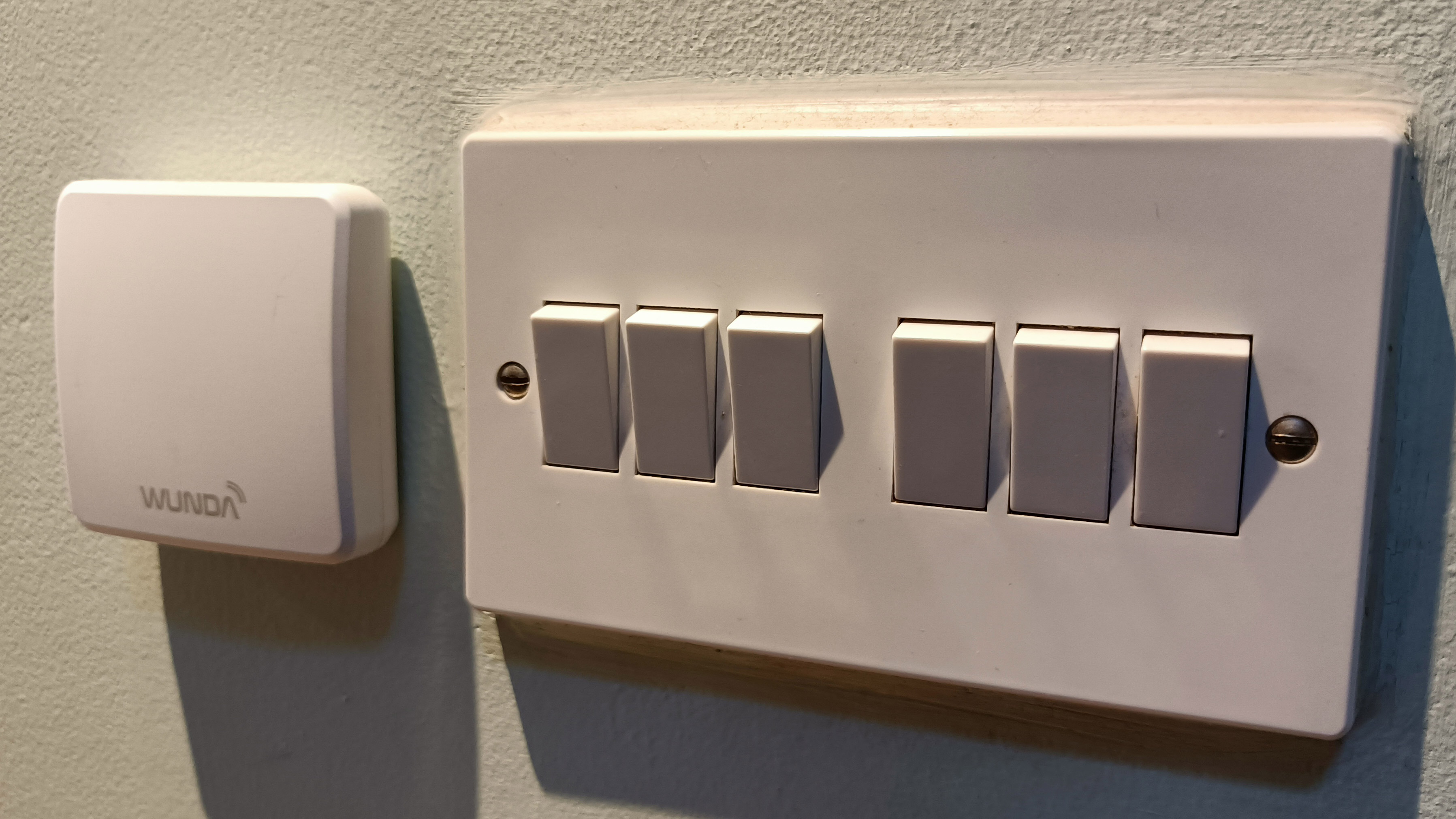 The screenless thermostat of the Wunda WundaSmart positioned on a wall next to a light switch