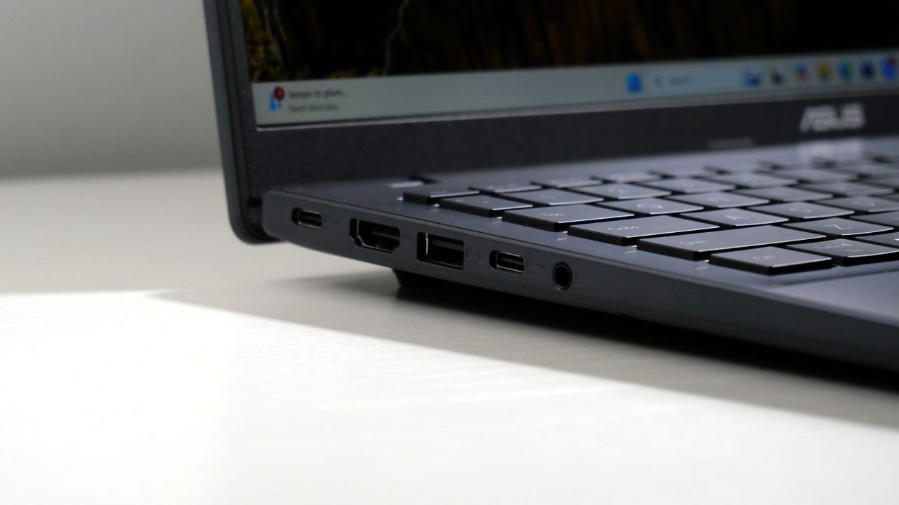 Asus Vivobook 16 (2025) open and powered on, highlighting the ports on the left side, which includes two USB Type-C, one USB Type-A, an HDMI, and headphone jack.