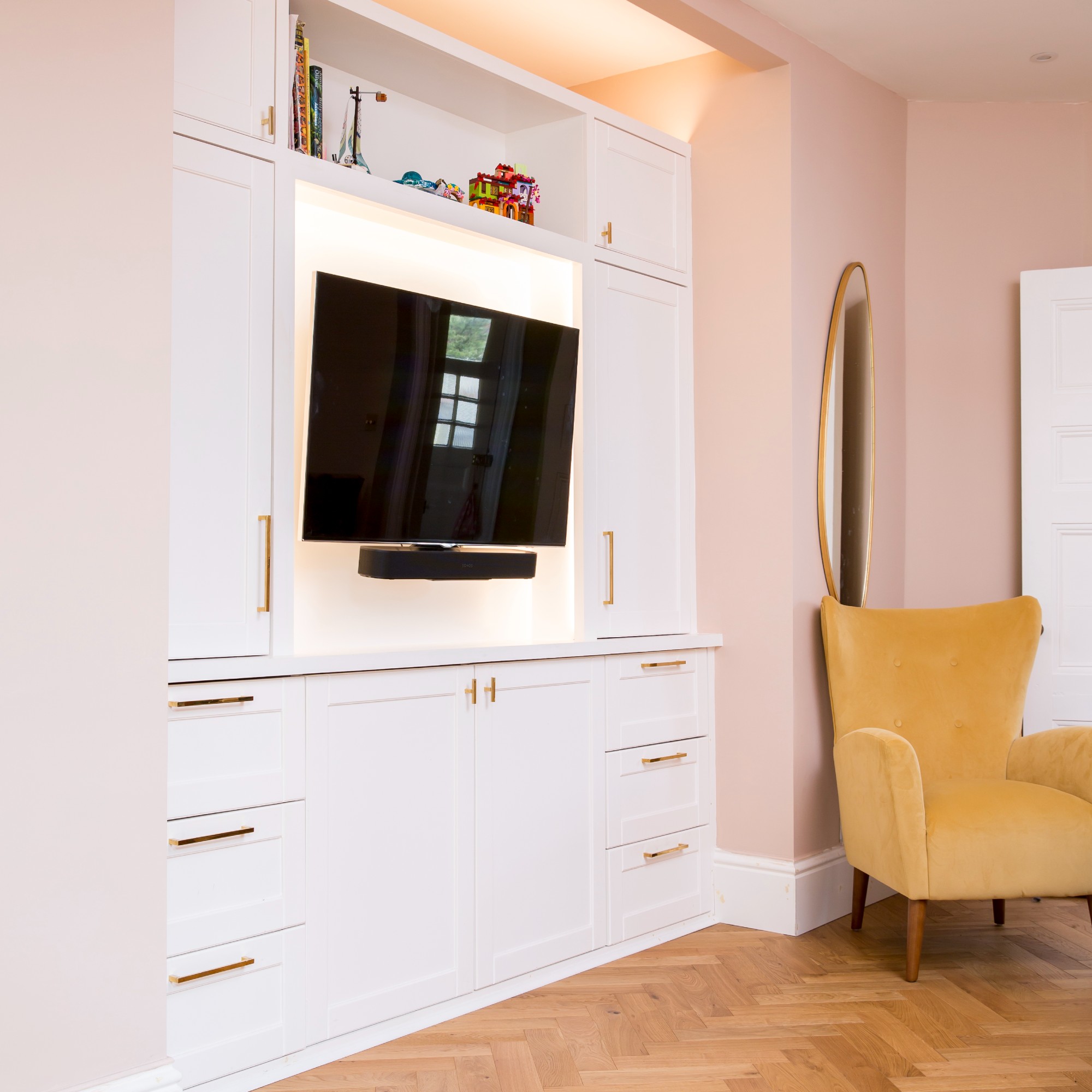 A pink-painted living room with a white built-in media unit featuring a TV