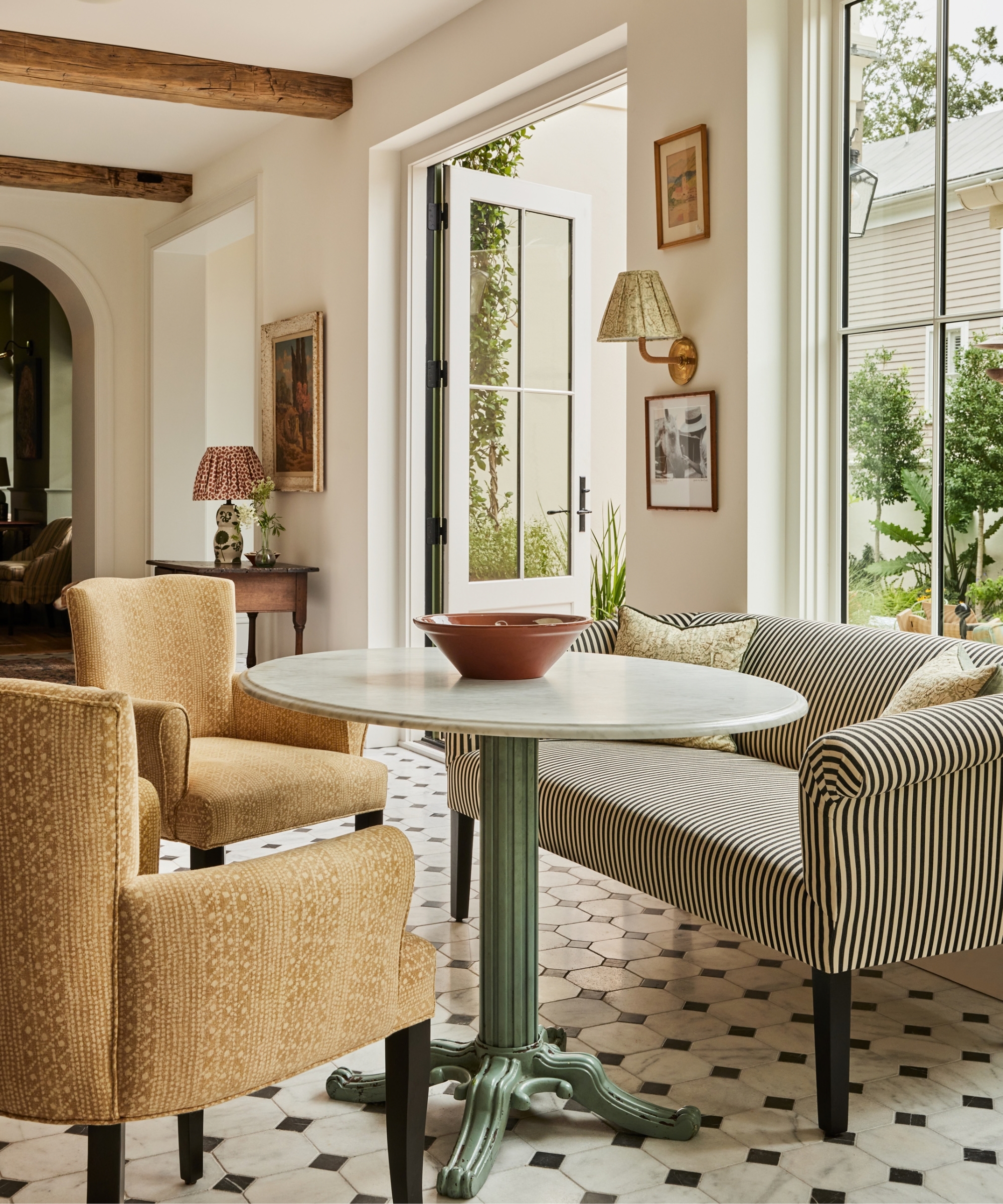 A kitchen seating area with a striped loveseat, two yellow armchairs, and a round marble tabletop on a white pillar-style base