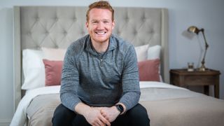 Greg Rutherford sits on a stylish bed with beige fabric headboard
