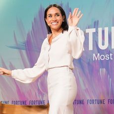 Meghan Markel walks off stage wearing a white pencil skirt and blouse with nude ankle strap heels.