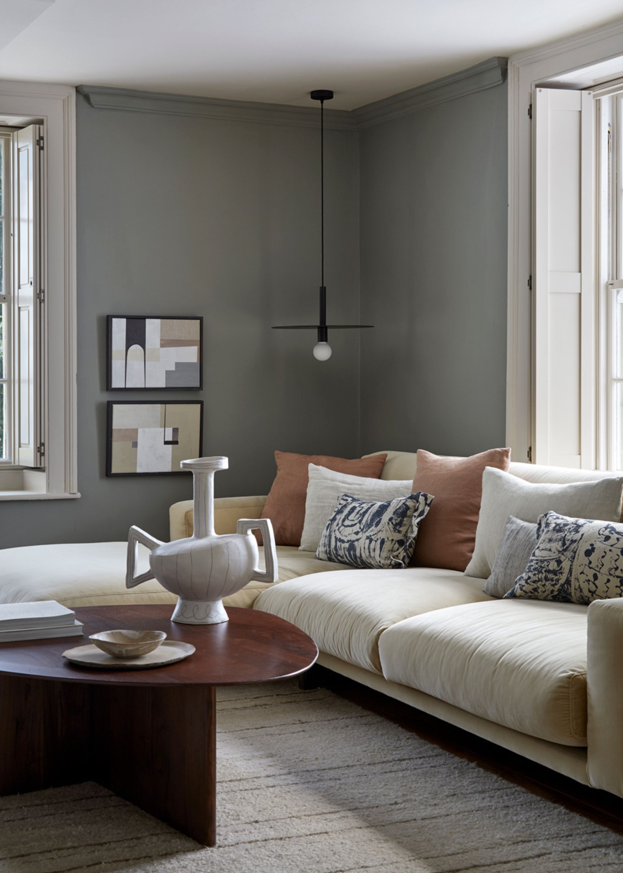 A living room with gray walls, a beige sofa with neutral and blush cushions, a cream rug, and a dark wooden coffee table.