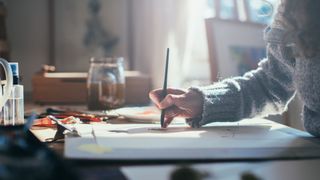 Woman painting at home on desk with sunlight coming through the window