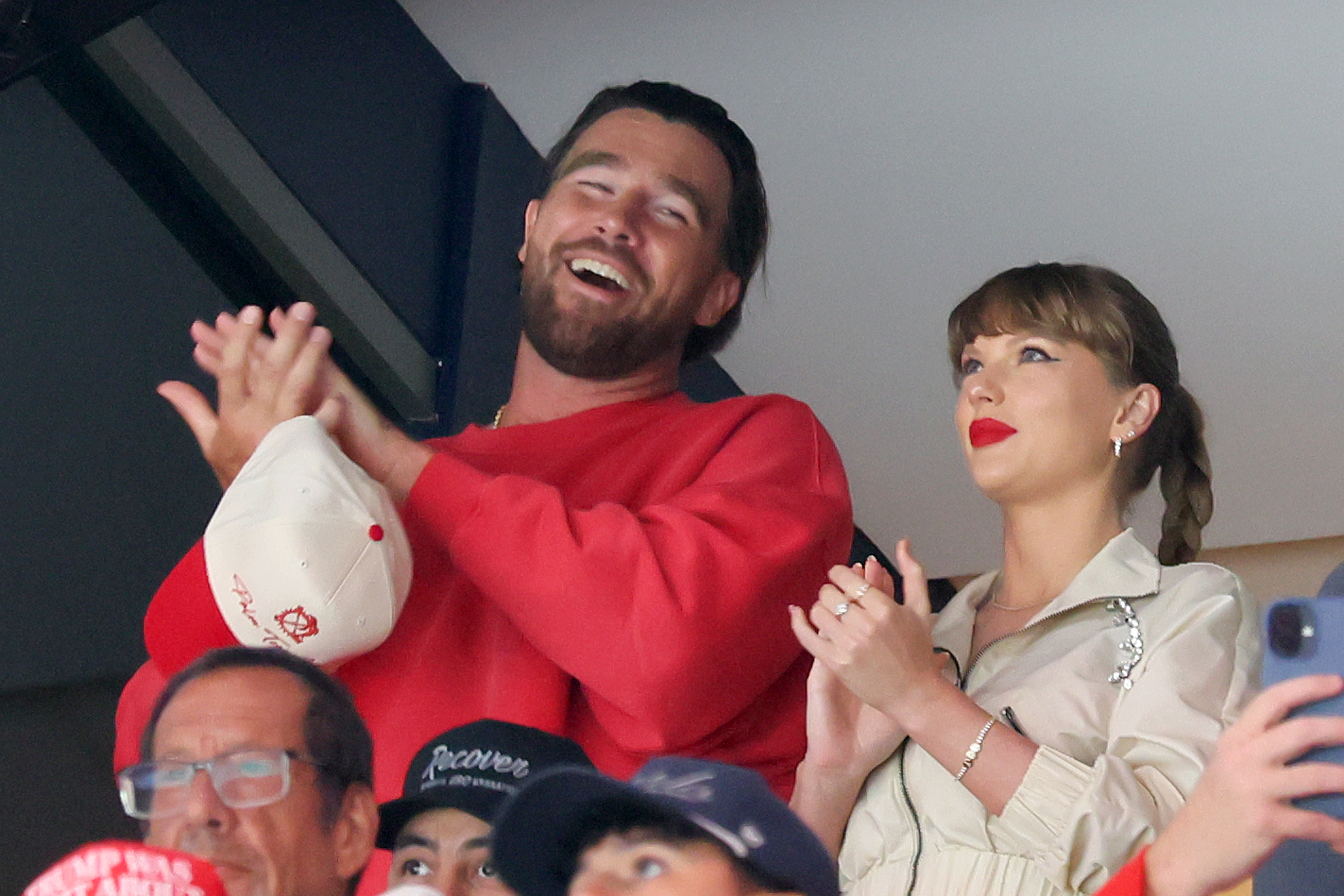 Travis Kelce in a red sweatshirt and Taylor Swift in a beige jacket watching the Edmonton Oilers and the Florida Panthers play during the first period in Game Four of the 2025 Stanley Cup Final at Amerant Bank Arena on June 12, 2025 in Sunrise, Florida