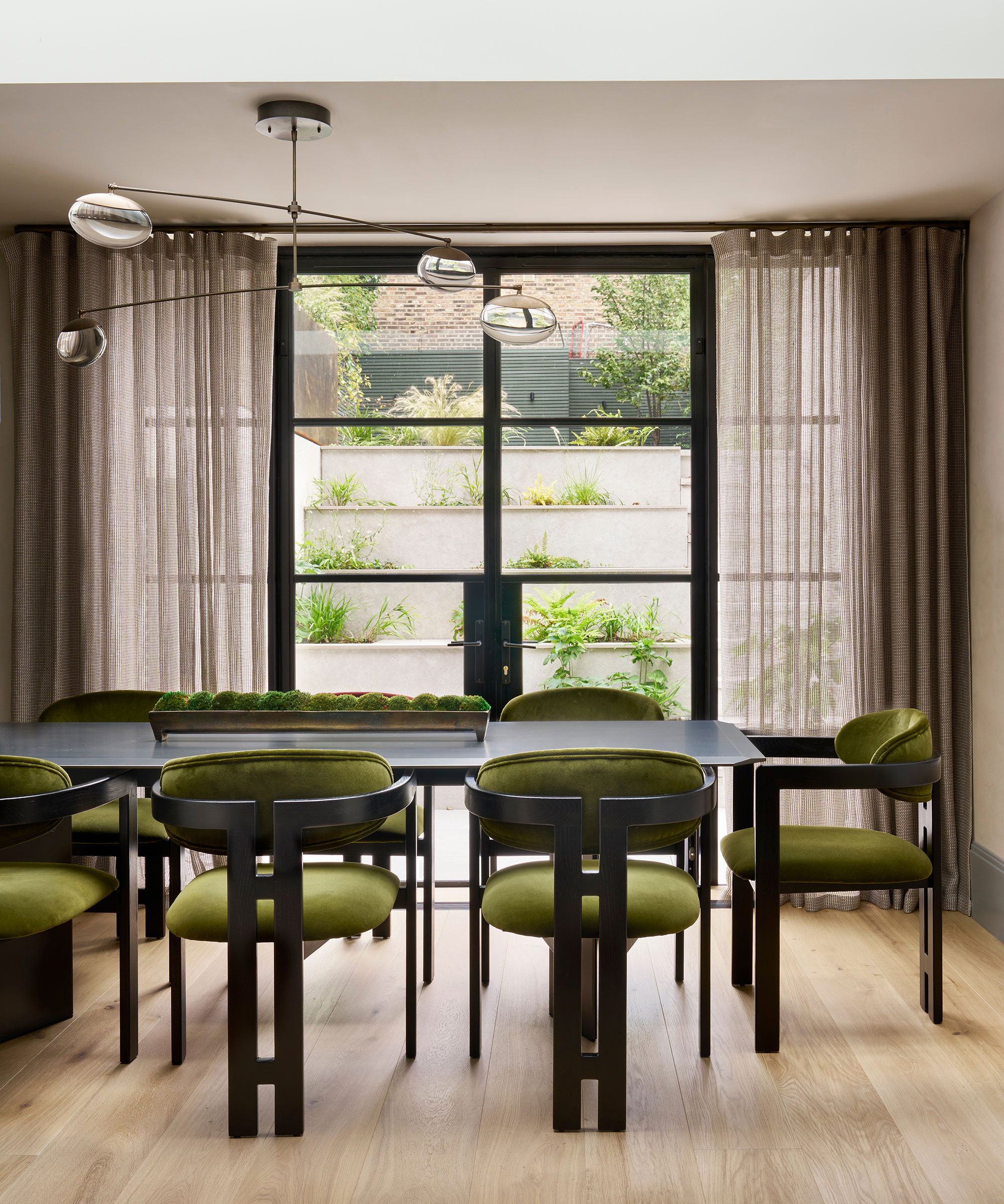 retro dining room with wooden flooring and green statement dining chairs with metal French doors