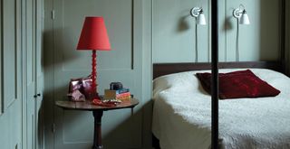 sage green painted bedroom with a four poster bed with red accessories