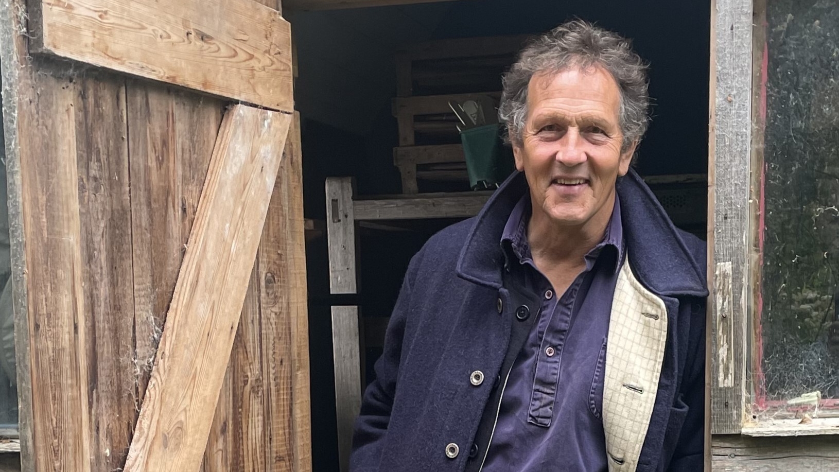 Monty Don standing in the doorway of a shed wearing a blue coat and green wellies for The RHS Chelsea Flower Show 2025