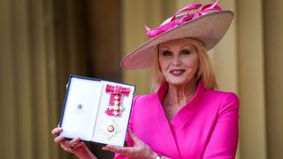 Joanna Lumley in a bright pink outfit posing with her DBE award in 2022