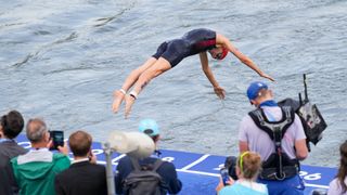 A single swimmer dives into the Seine river as a crowd and cameraman surround them